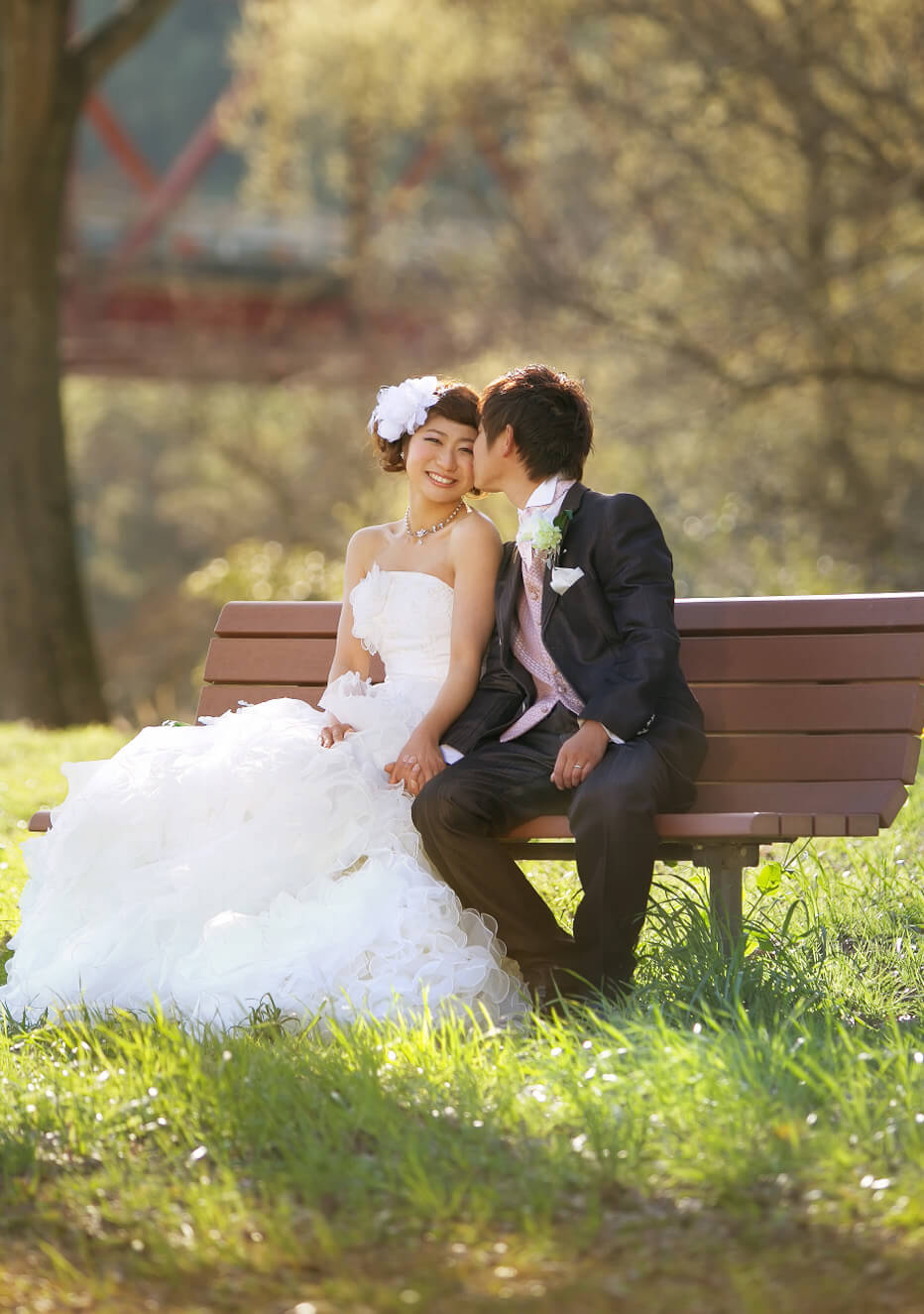 写真：ウェディングドレスを着た新婦とタキシードを着た新郎がベンチでくつろぐ様子